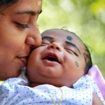 Heartwarming portrait of a mother kissing her smiling baby outdoors.